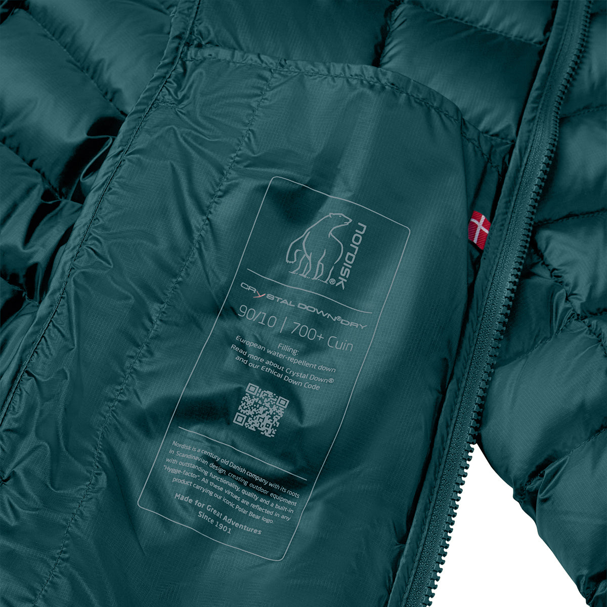 Close-up of a dark teal puffer jacket interior showing a sewn-in label for 'nordou' Crystal Alpha Foam 900g / 700G foam, with a zipper and a small red flag tag visible.