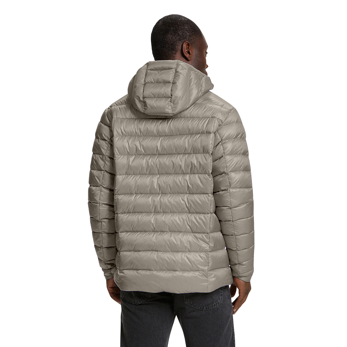 A man viewed from the back wearing a light taupe-gray hooded puffer jacket and dark gray jeans, set against a plain white background.