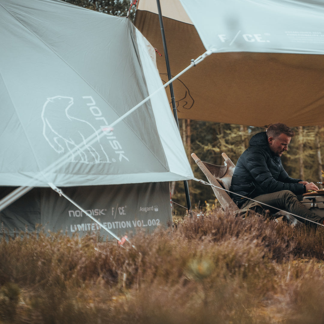 Person sitting under a tent with a visible brand logo in a natural setting