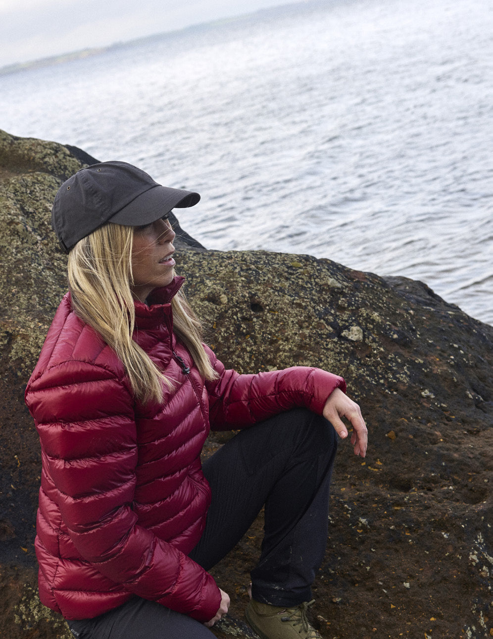 Frau in der Companyon Daunenjacke Thyra in Tibetan Red auf einem Felsen an der Küste