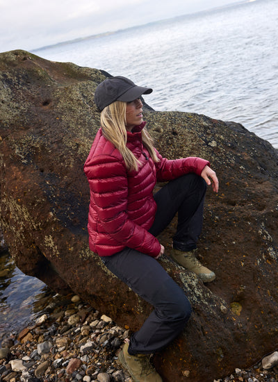 Frau in der Companyon Daunenjacke Thyra in Tibetan Red auf einem Felsen am Meer
